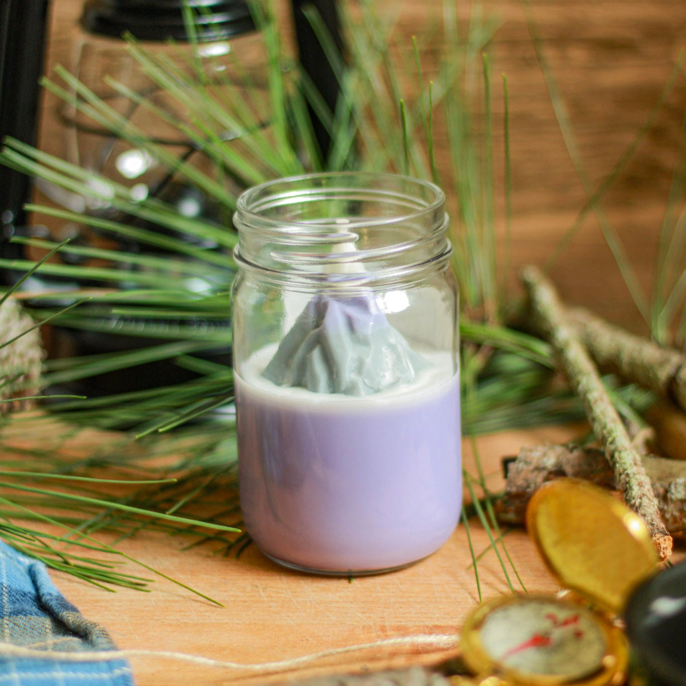 Purple candle in a mason jar with plants and a lantern in the background