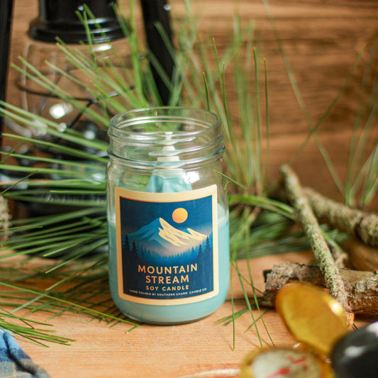 Candle jar labeled 'Mountain Stream' on a wooden surface with natural elements.